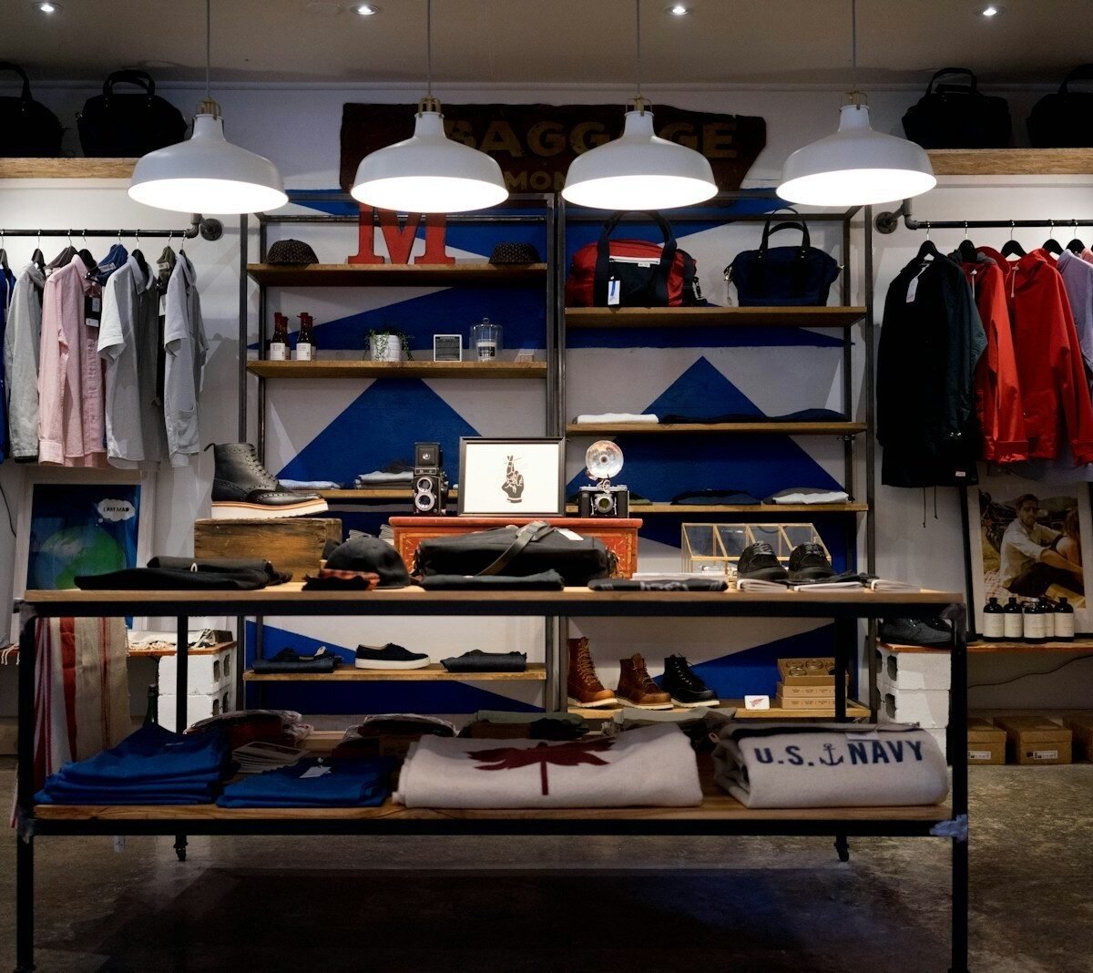 Interior de loja de moda com araras de roupas, prateleiras de madeira, bolsas e luminárias industriais