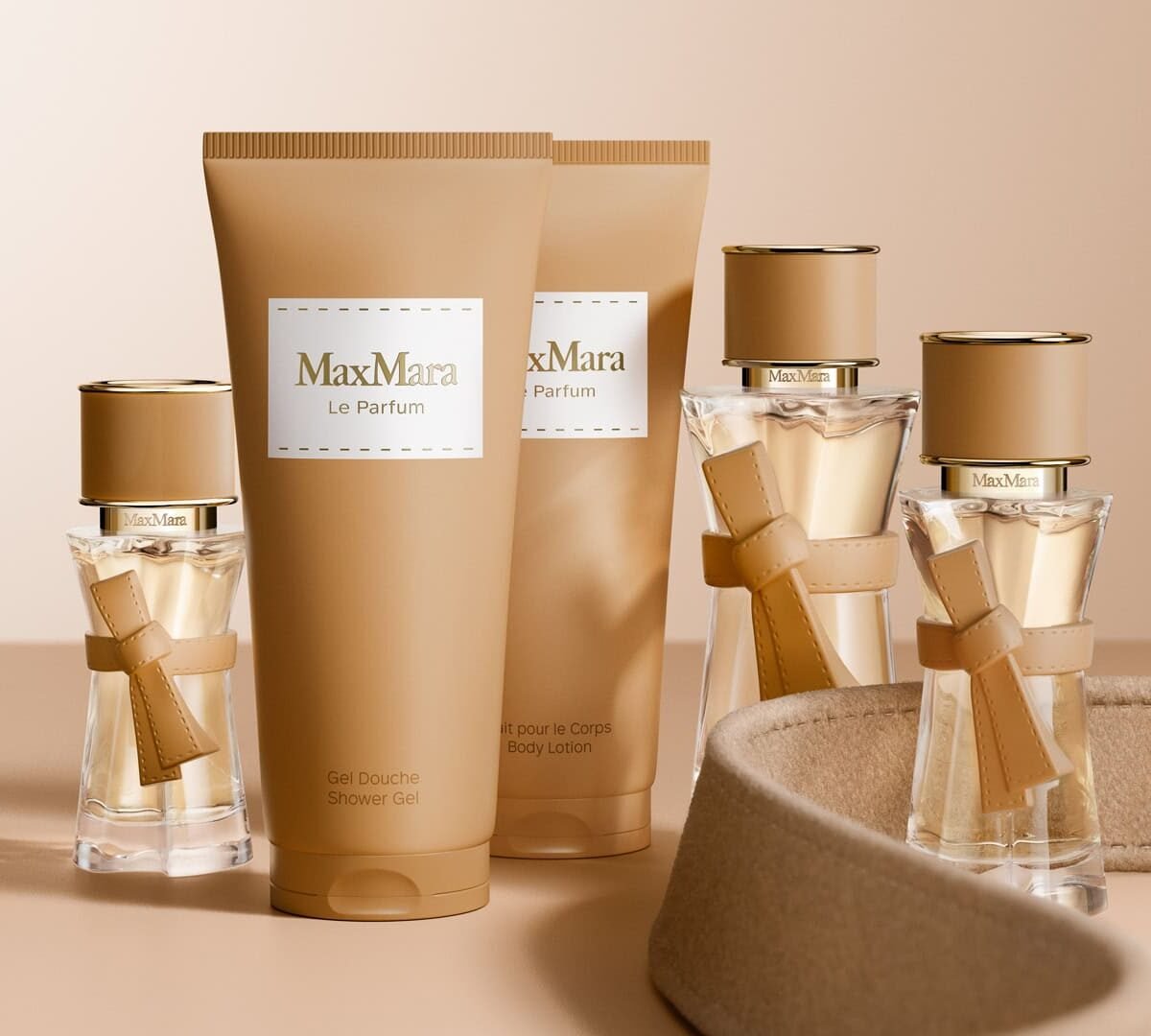 Frascos do perfume Le Parfum da Max Mara ao lado de gel de banho e loção corporal em embalagens bege, sobre fundo camel