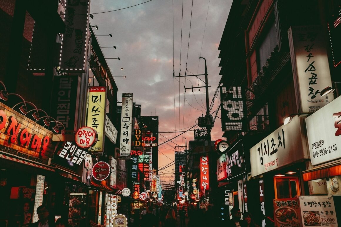 Rua comercial de Seul ao entardecer, com letreiros luminosos em coreano dos dois lados da via