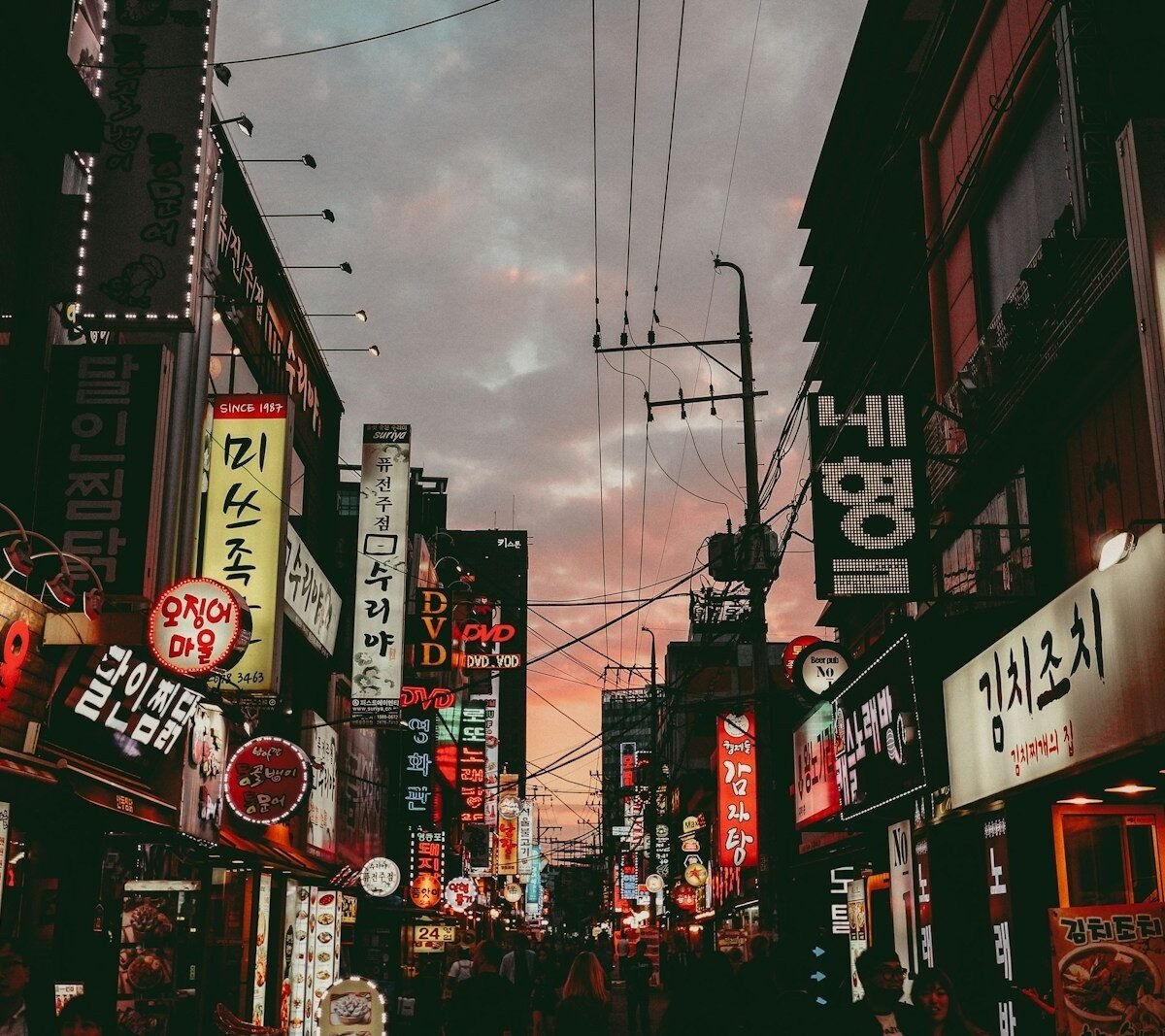 Rua comercial de Seul ao entardecer, com letreiros luminosos em coreano dos dois lados da via