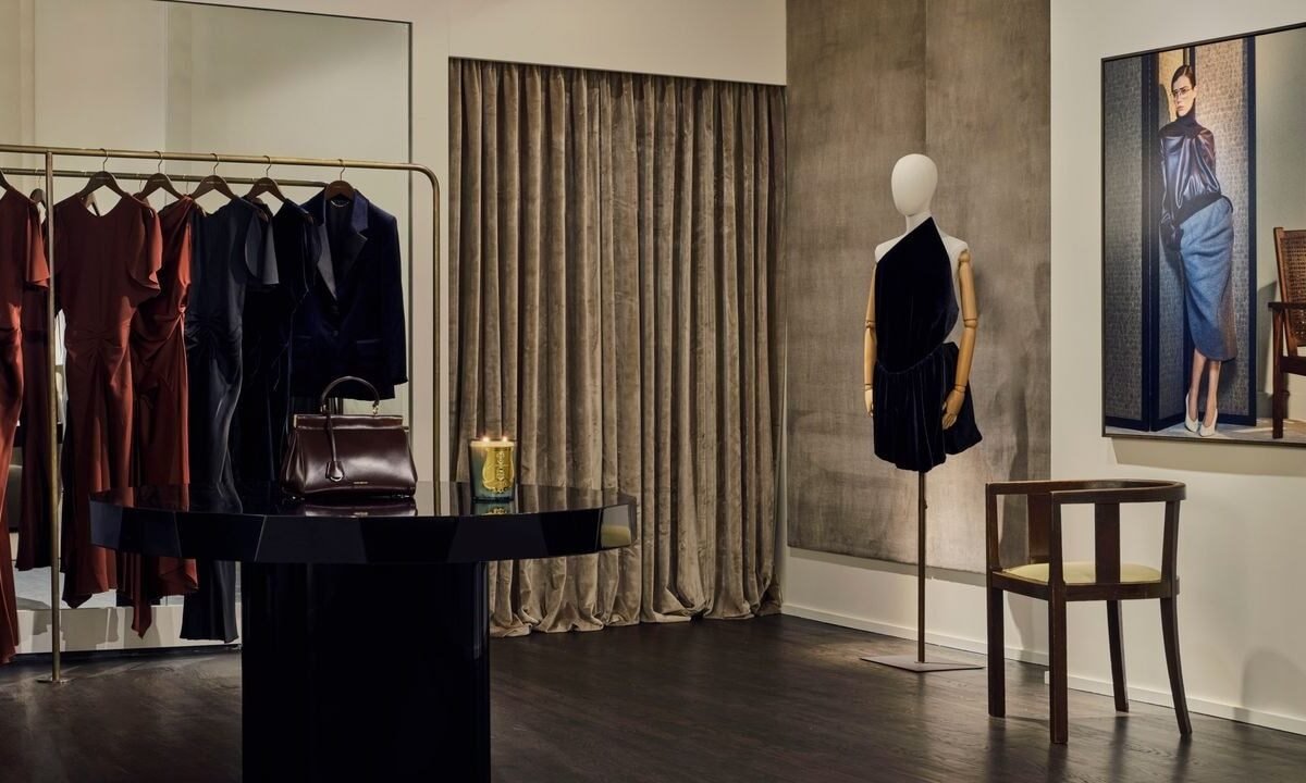 Interior da loja com arara de vestidos, bolsa sobre mesa central preta, manequim com vestido de veludo e quadro na parede
