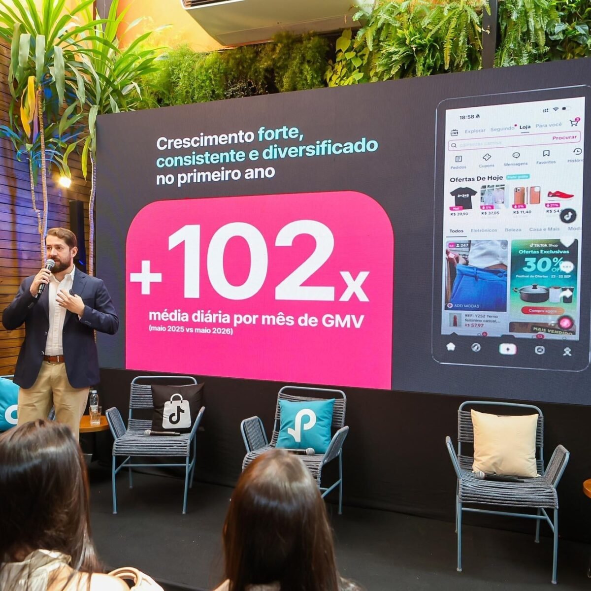 Executivo fala ao microfone diante de painel do TikTok Shop com dados de crescimento e tela do aplicativo, em evento com plateia