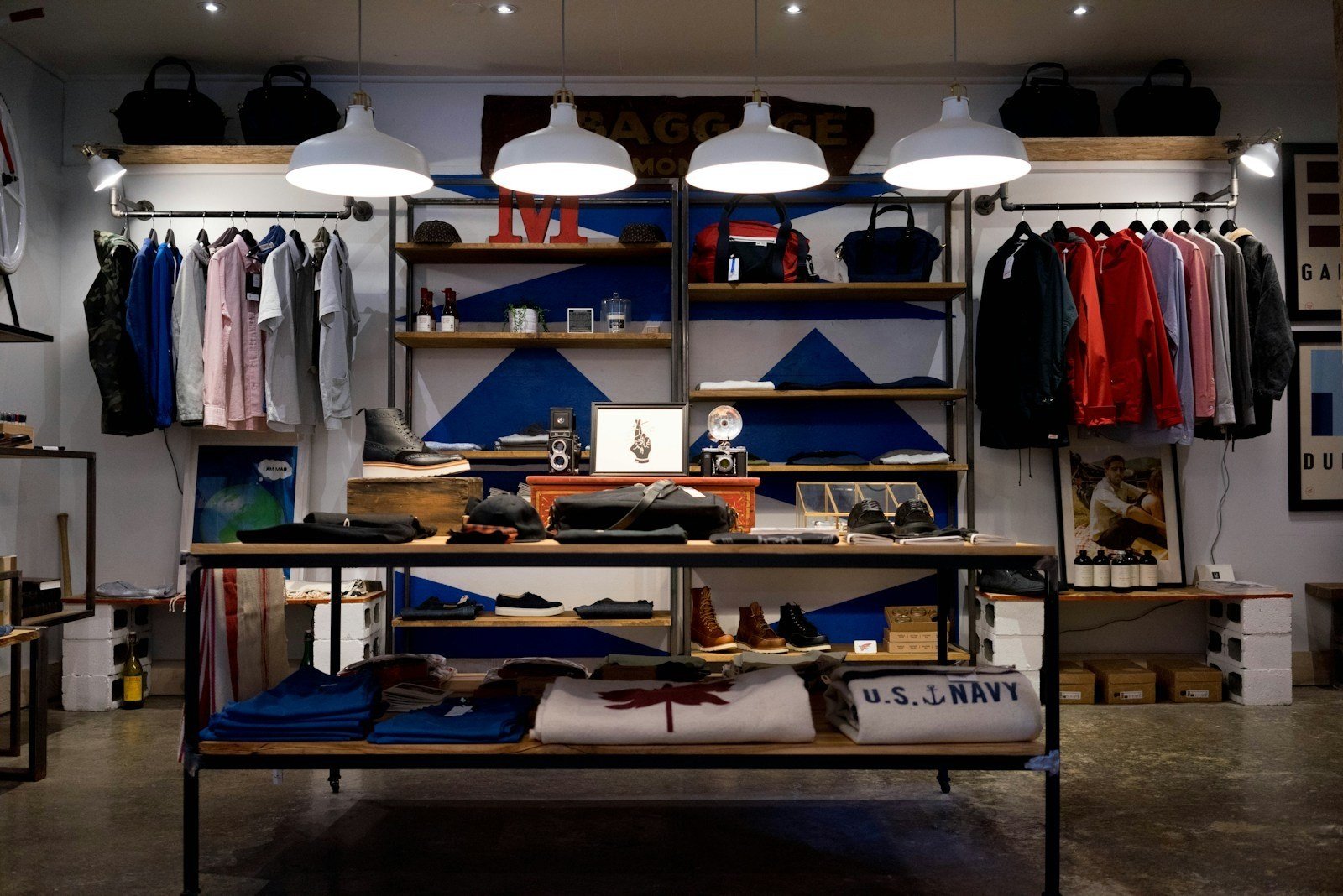 Interior de loja de moda com araras de roupas, prateleiras de madeira, bolsas e luminárias industriais