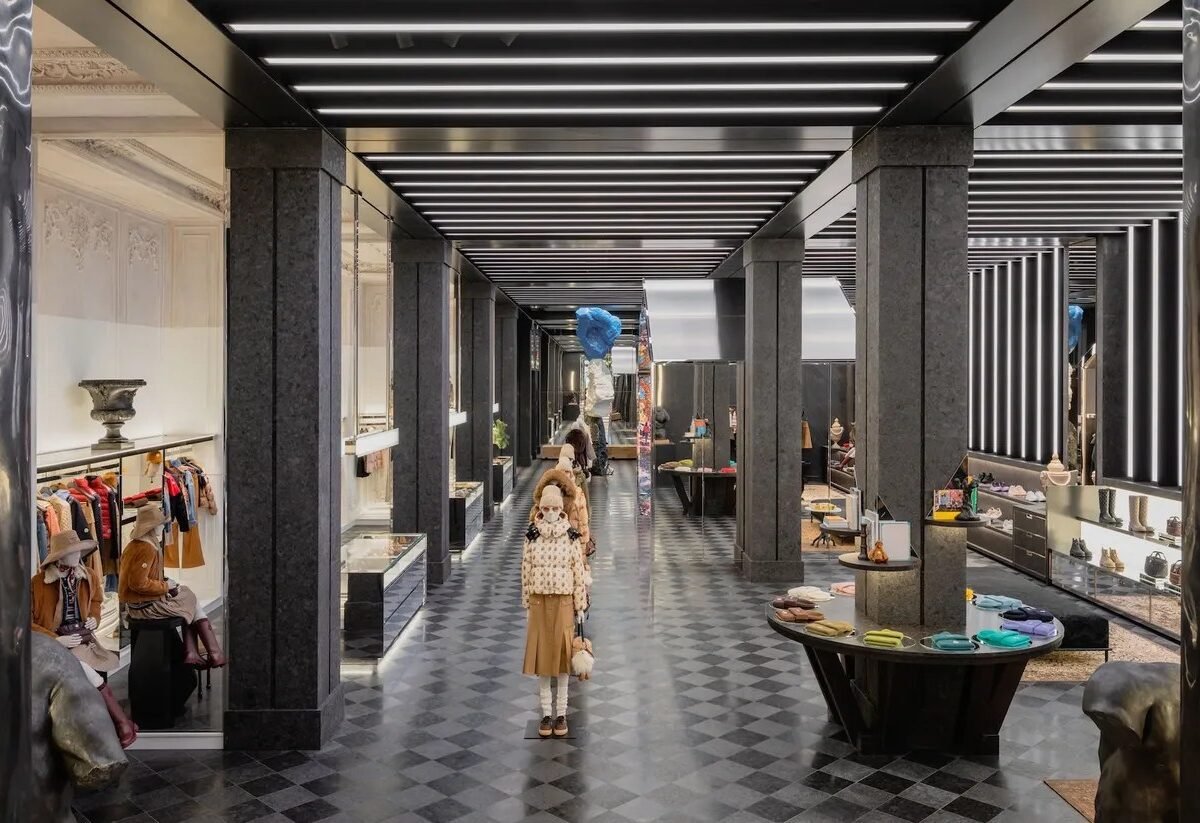 Interior da flagship com piso xadrez de mármore, colunas escuras, teto de luzes lineares e manequins com peças da coleção
