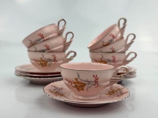 Conjunto de xícaras e pires de porcelana rosa-claro com motivos florais e filetes dourados, empilhados sobre superfície branca