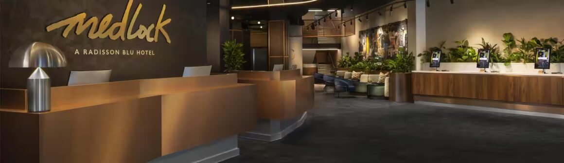 Lobby de hotel com balcão de recepção em tom bronze e letreiro Medlock em dourado na parede
