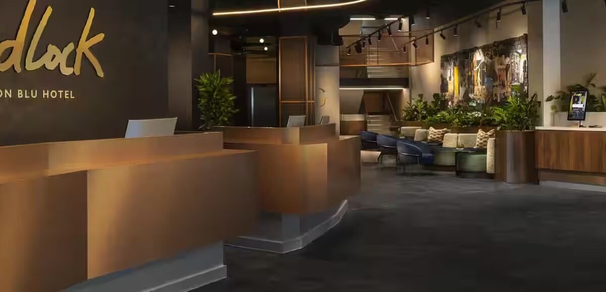 Lobby de hotel com balcão de recepção em tom bronze e letreiro Medlock em dourado na parede