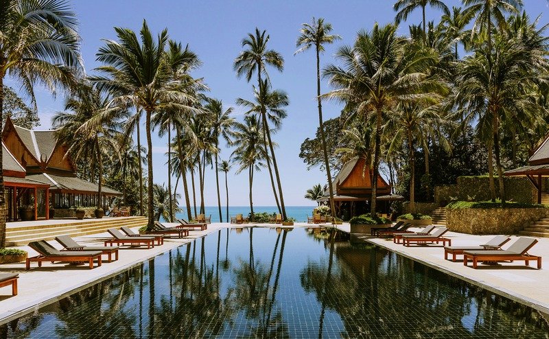 Piscina do Amanpuri cercada por coqueiros e pavilhões de madeira, com vista para o mar em Phuket.