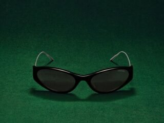 Óculos escuros Prada de armação preta e hastes finas de titânio sobre fundo verde.