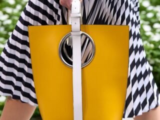 Modelo com saia plissada preta e branca carregando bolsa tote amarela com argola metálica.
