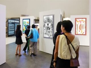 Visitantes observam obras exibidas em televisores com molduras coloridas em sala de exposição.