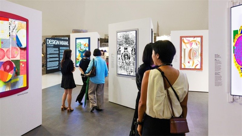 Visitantes observam obras exibidas em televisores com molduras coloridas em sala de exposição.