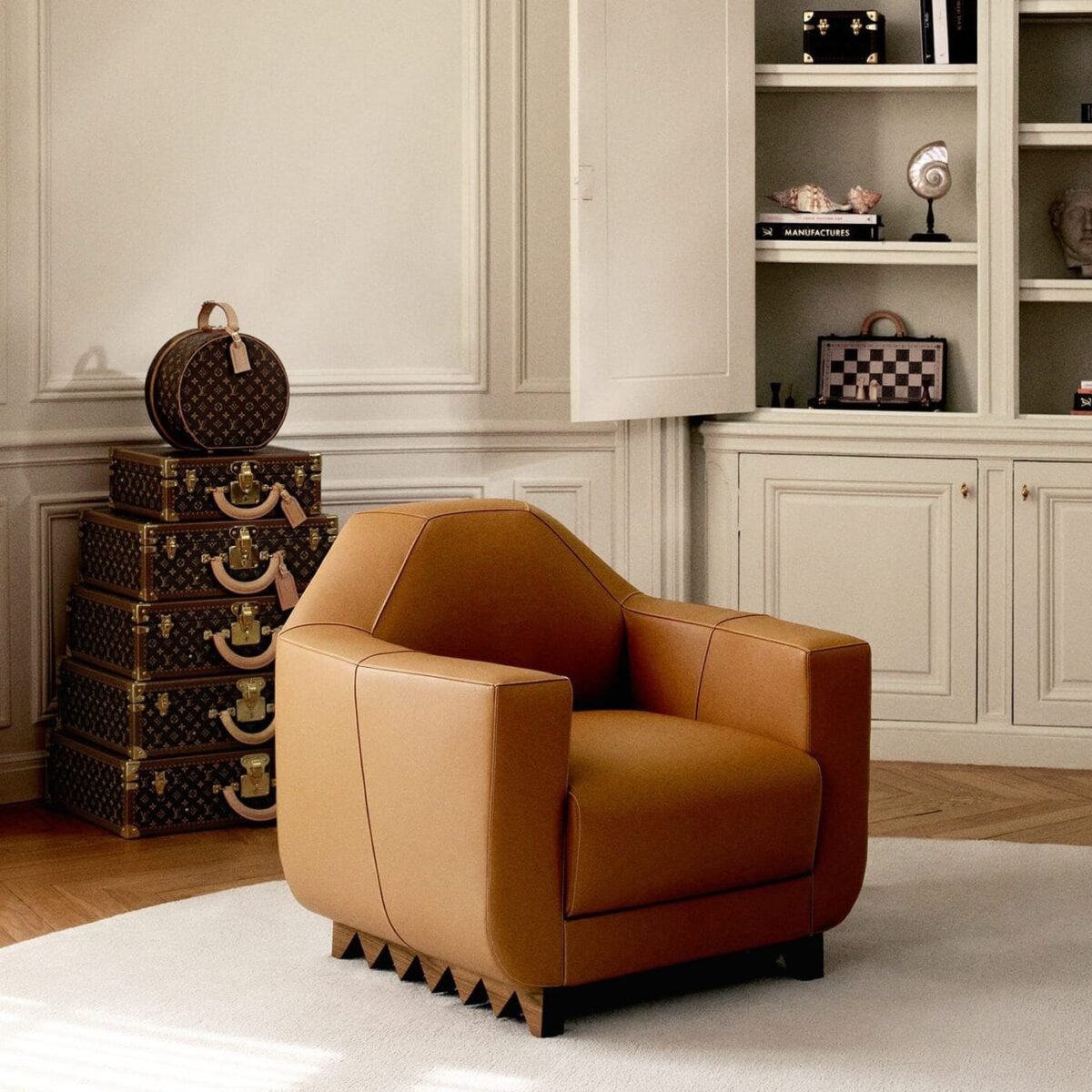 Poltrona de couro caramelo em sala clara, ao lado de baús Louis Vuitton empilhados