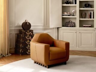 Poltrona de couro caramelo em sala clara, ao lado de baús Louis Vuitton empilhados
