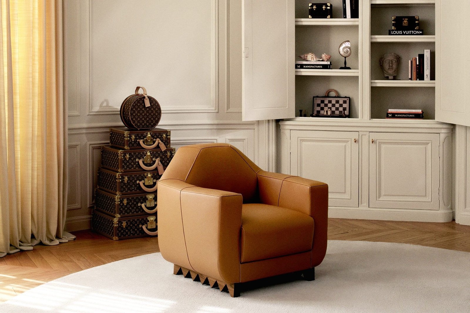 Poltrona de couro caramelo em sala clara, ao lado de baús Louis Vuitton empilhados