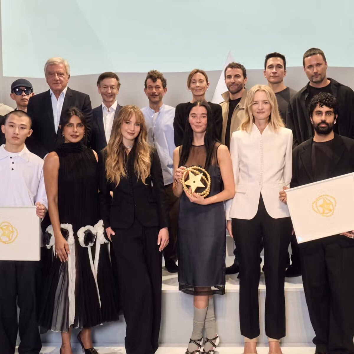 Grupo de jurados e premiados posa no palco da final do Prêmio LVMH, com dois finalistas segurando diplomas