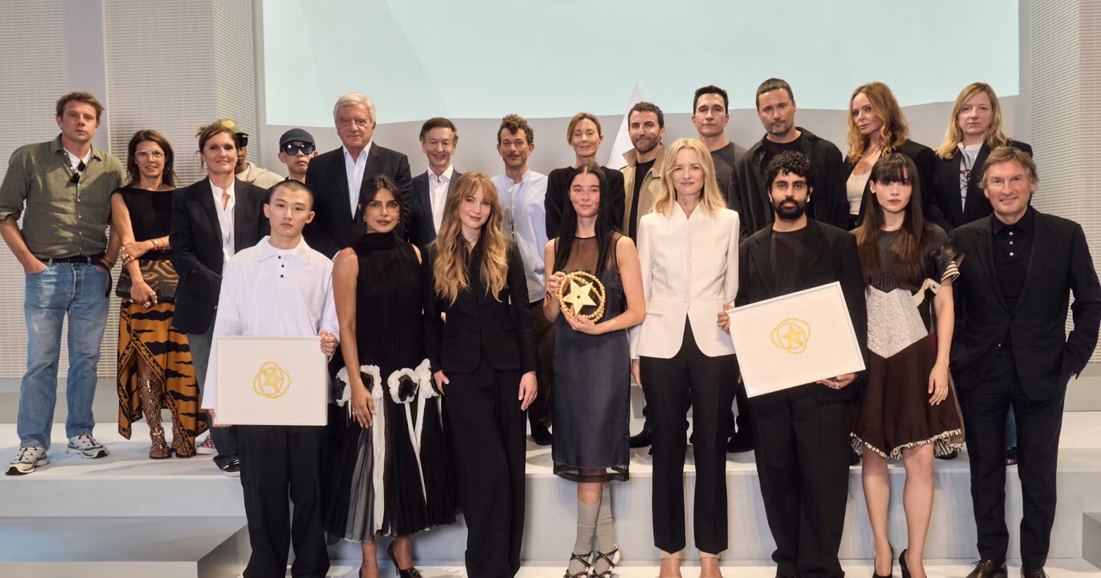 Grupo de jurados e premiados posa no palco da final do Prêmio LVMH, com dois finalistas segurando diplomas