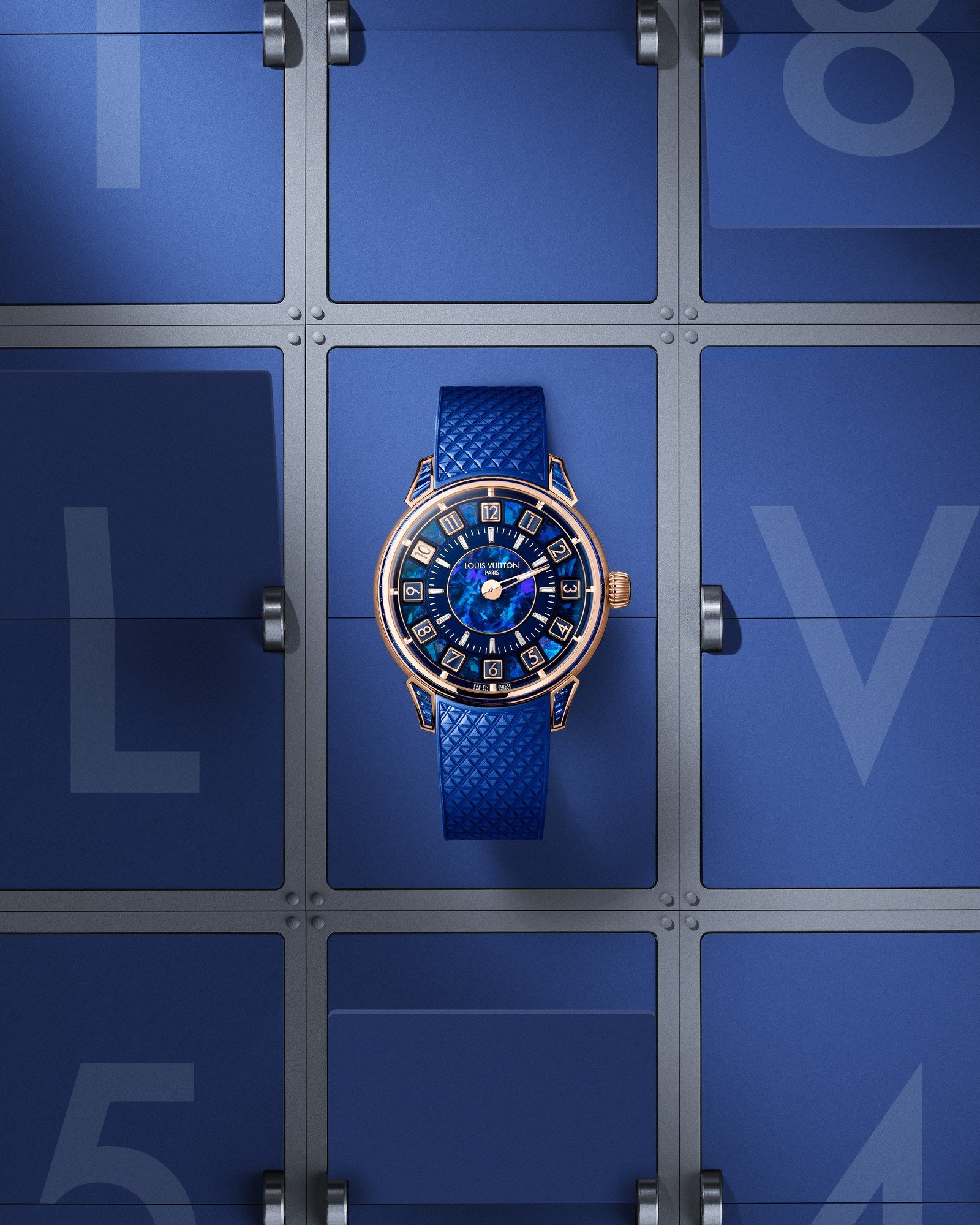 Relógio Tambour Spin Time de caixa em ouro rosa, com mostrador azul, doze cubos giratórios com numerais em volta de um centro em opala azul iridescente e pulseira azul texturizada, sobre fundo azul que imita um painel de aeroporto com as letras L e V