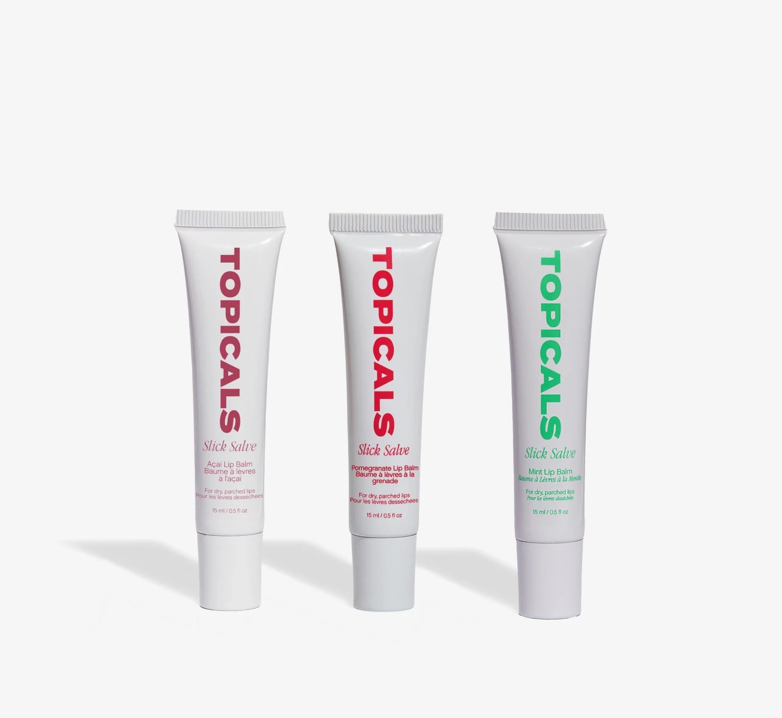 Três bisnagas brancas do lip balm Slick Salve da Topicals, nas versões açaí, romã e menta, em fundo claro