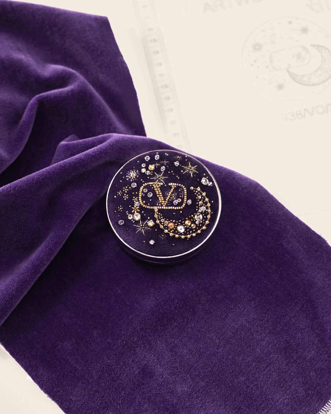 Compacto roxo bordado com motivo celeste sobre tecido de veludo.