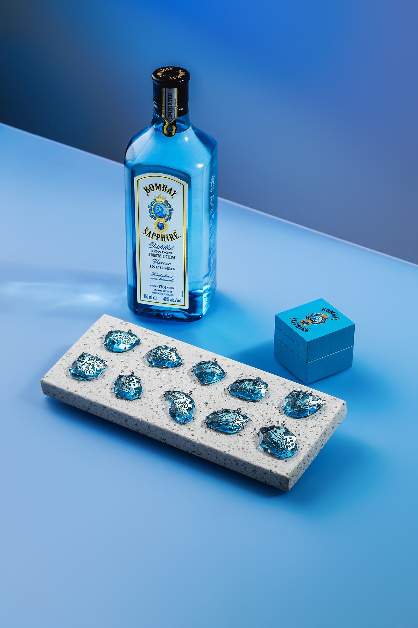 Os dez pingentes em vidro azul reciclado ao lado de uma garrafa de Bombay Sapphire.