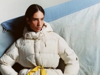 Modelo veste jaqueta acolchoada branca da coleção Moncler Re/Icons 2026, com faixa amarela na cintura.