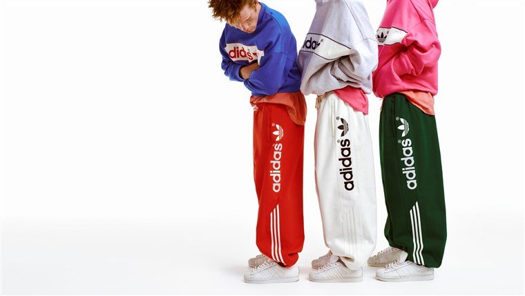 Três modelos com moletons e calças amplas vermelha, branca e verde da linha adiSignature, da Adidas Originals