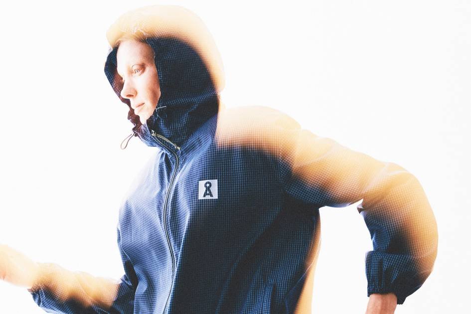 Mulher veste jaqueta corta-vento azul com capuz da Armedangels, em imagem com efeito de luz