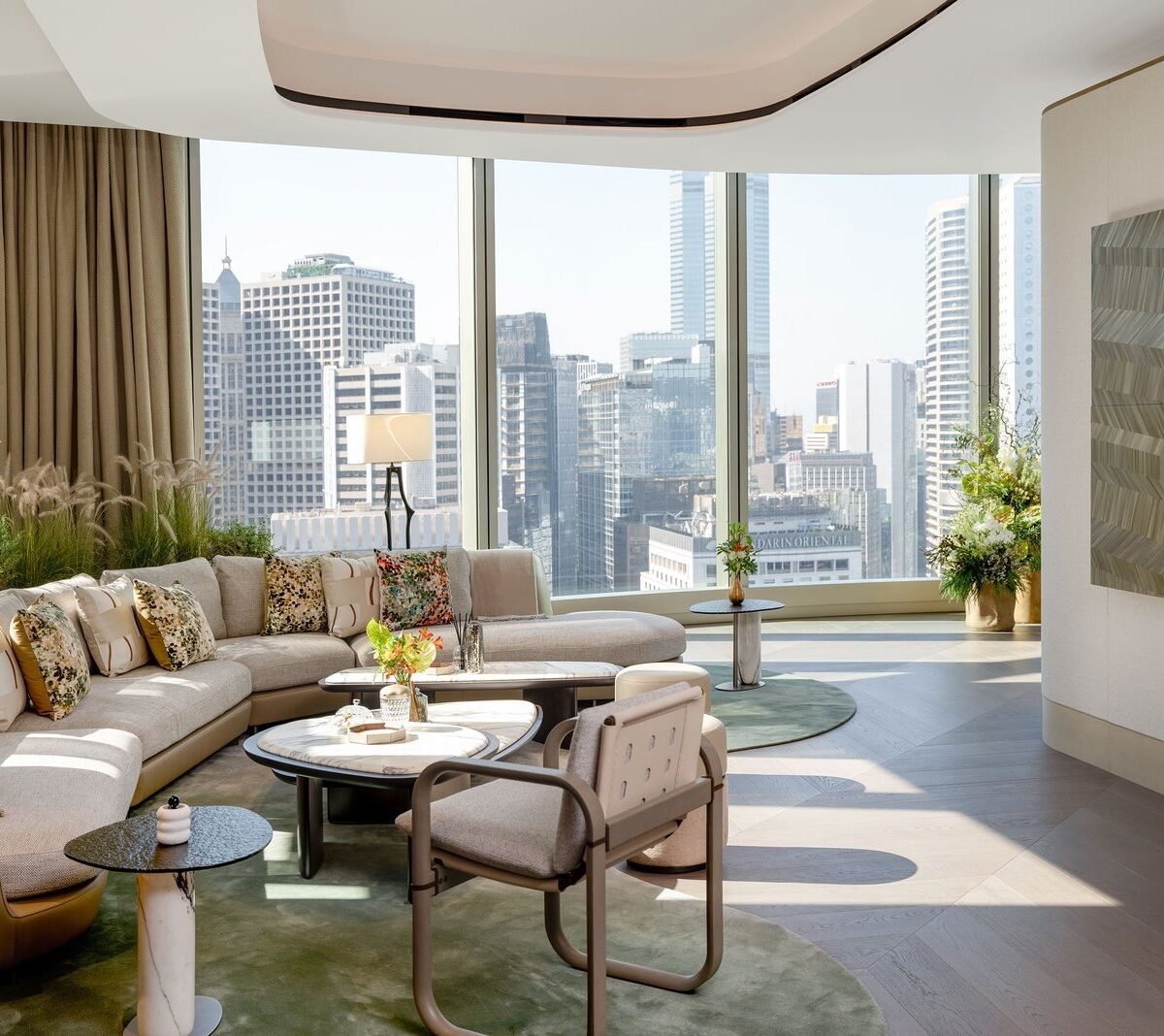 Sala de estar com sofá curvo, mesas de mármore e janelas com vista para os prédios de Hong Kong