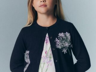 Menina de cardigã azul-marinho bordado com flores lilás sobre blusa estampada, da coleção Bonpoint x MoMA