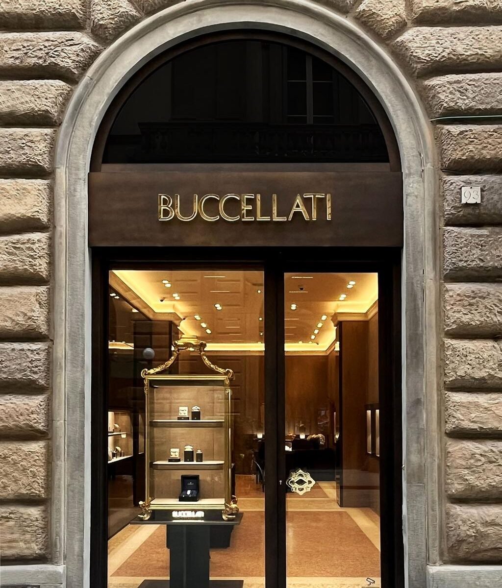 Fachada em arco da boutique Buccellati na Via Tornabuoni, em Florença, com vitrine iluminada.