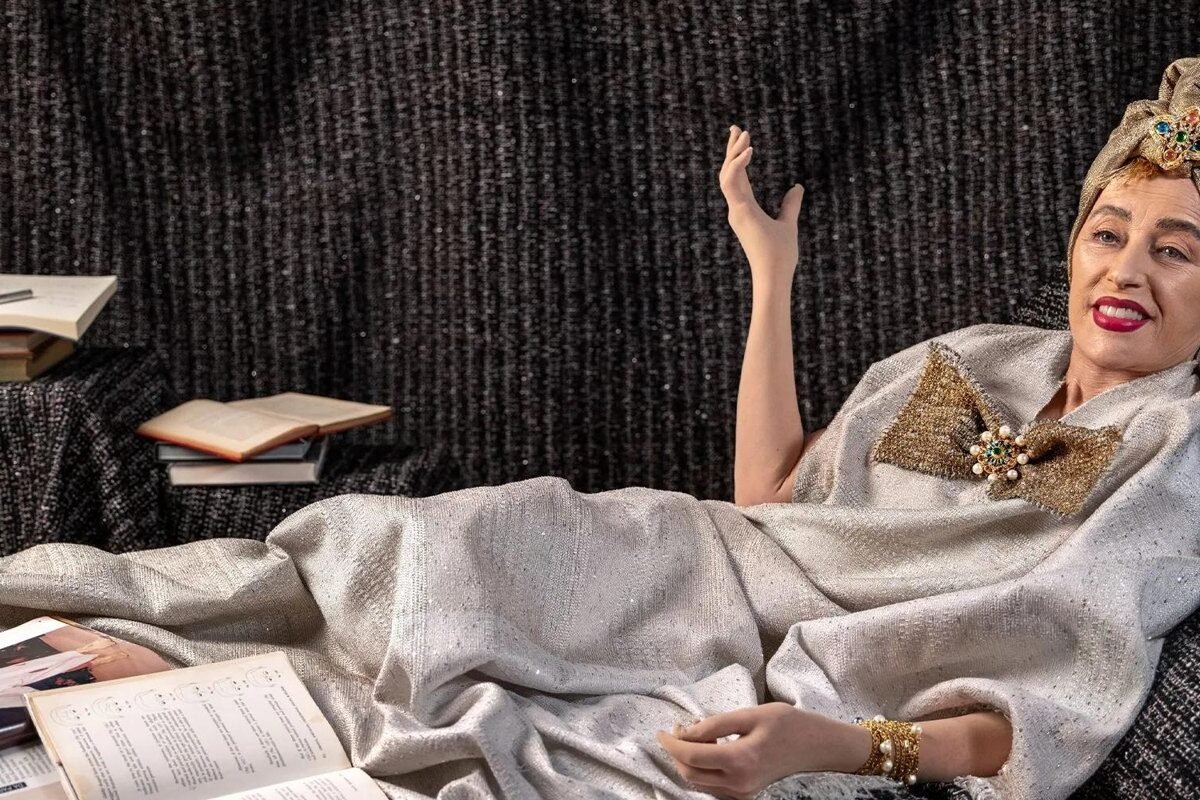 Personagem criada por Cindy Sherman com turbante dourado e tecidos drapeados, recostada em um sofá