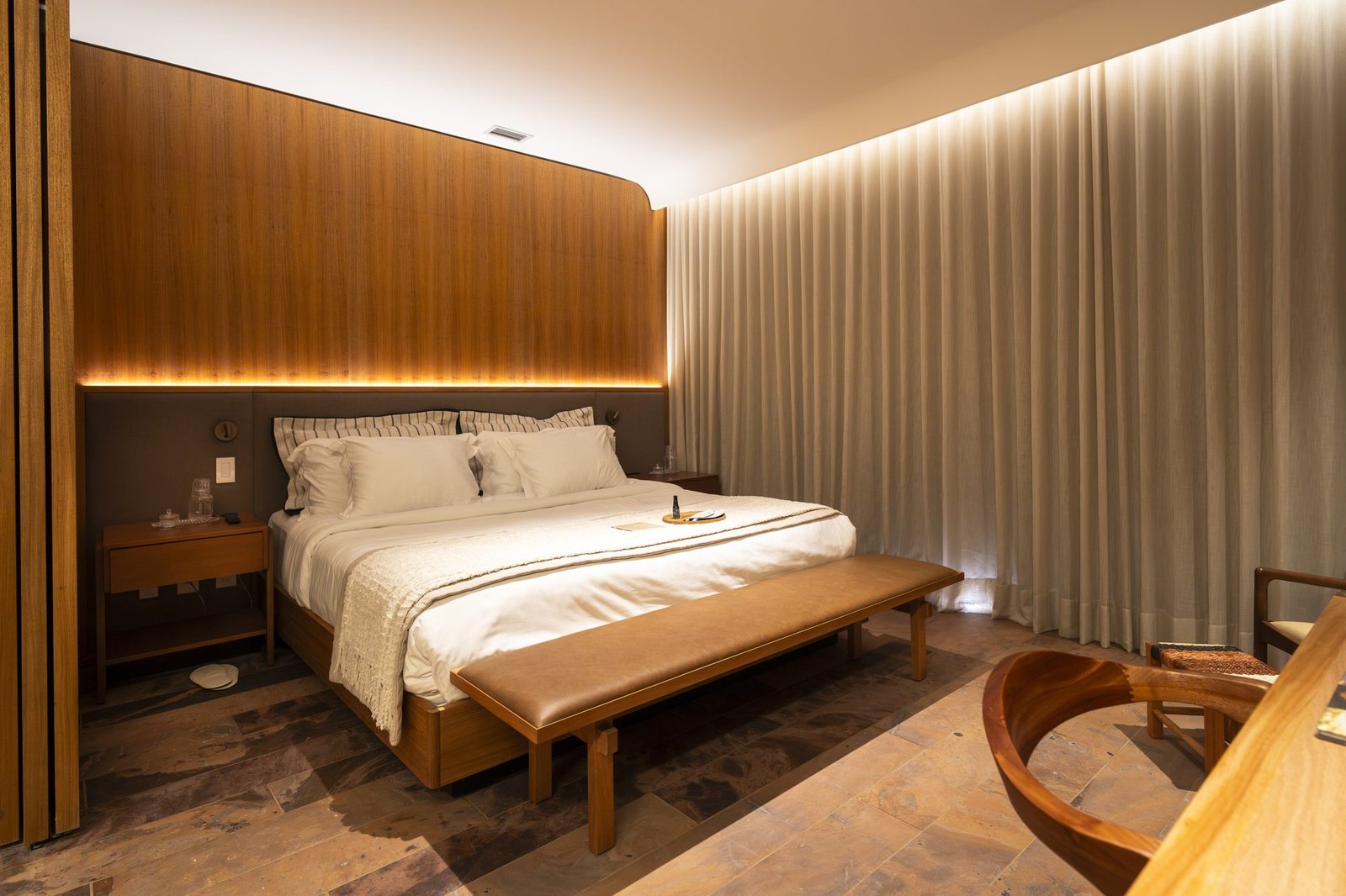 Quarto do Clara Arte com cabeceira em madeira iluminada, cama king-size e banco de couro