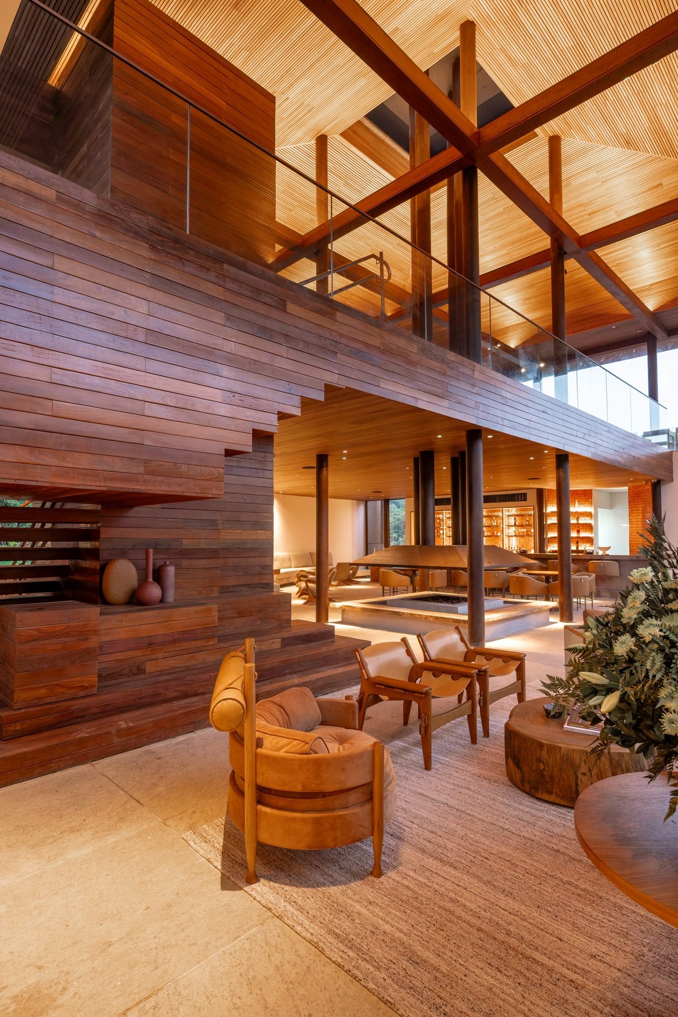 Lobby do Clara Arte com escada escultural de madeira, pé-direito alto e poltronas de couro