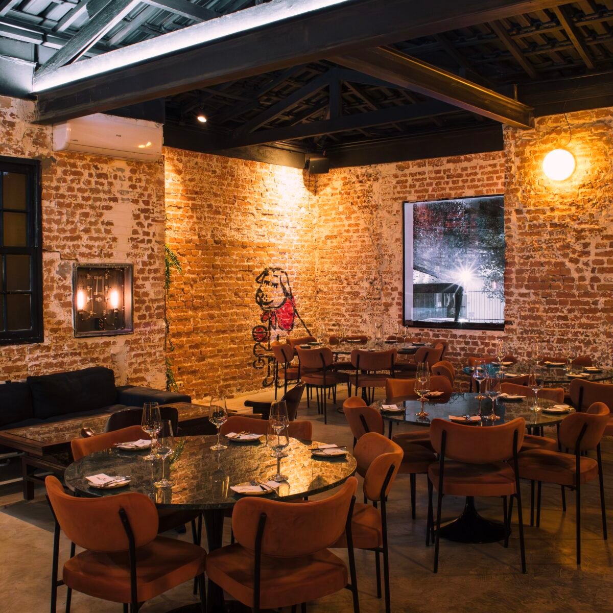 Salão do Clementina Bar de Vinhos, em Pinheiros, com paredes de tijolo aparente e mesas redondas.