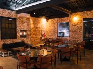 Salão do Clementina Bar de Vinhos, em Pinheiros, com paredes de tijolo aparente e mesas redondas.