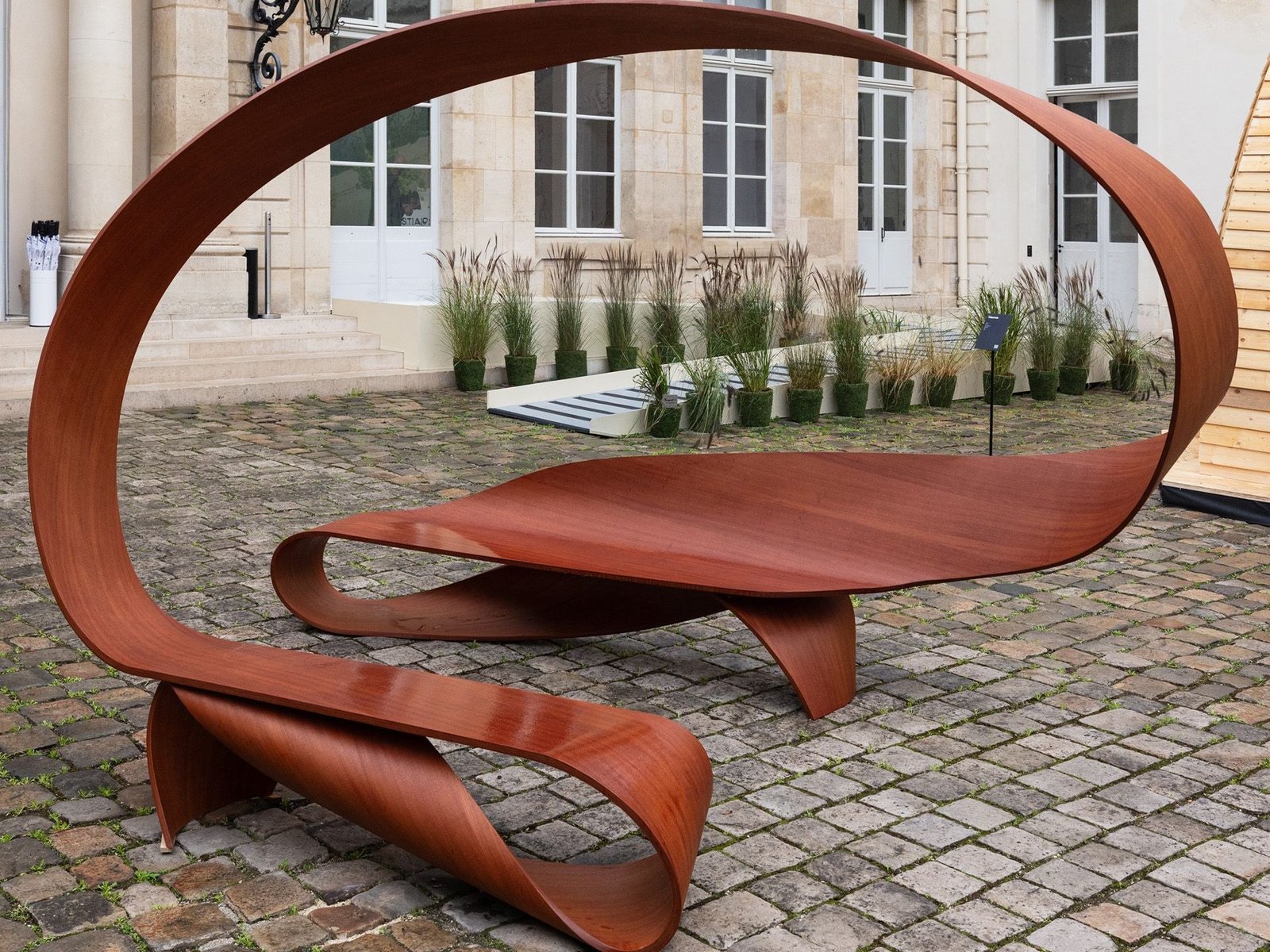 Banco Arabesque, de Pierre Renart, em madeira moabi no jardim do Hôtel de Maisons durante a Design Miami.Paris