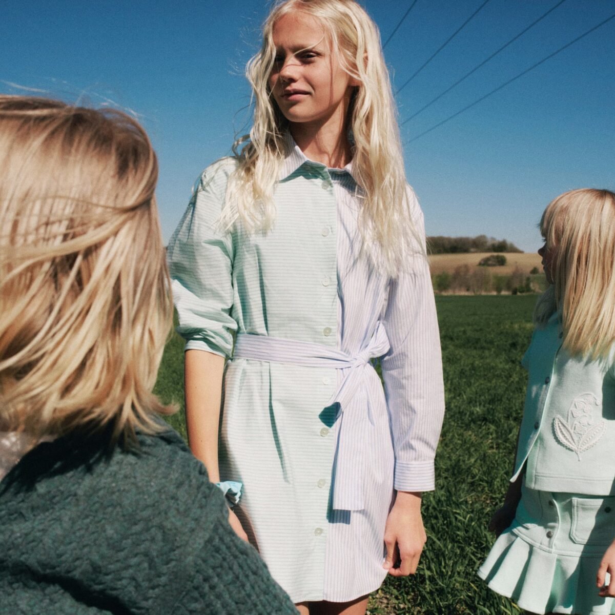 Meninas com vestidos e peças em verde-claro e branco da coleção Versailles Beach, da Dior, em um campo sob céu azul
