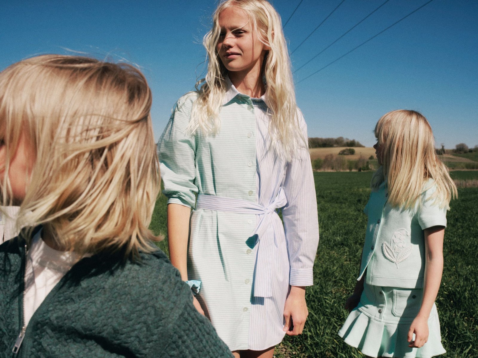 Meninas com vestidos e peças em verde-claro e branco da coleção Versailles Beach, da Dior, em um campo sob céu azul