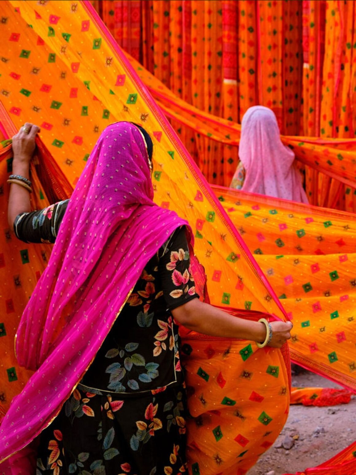 Mulheres com véus coloridos estendem tecidos laranja estampados para secar, na Índia