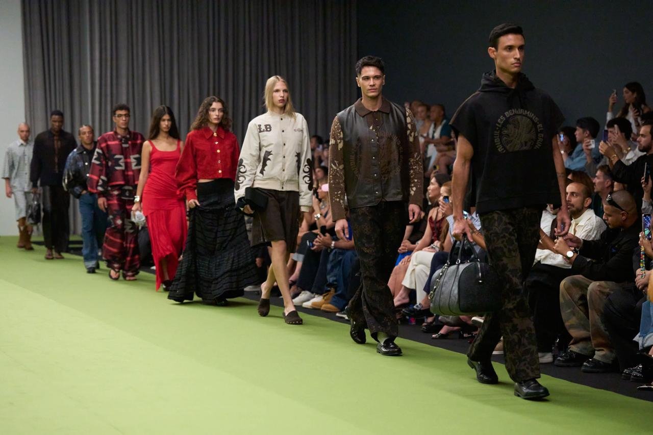 Fila de modelos na passarela verde da Dubai Fashion Week, com plateia ao lado