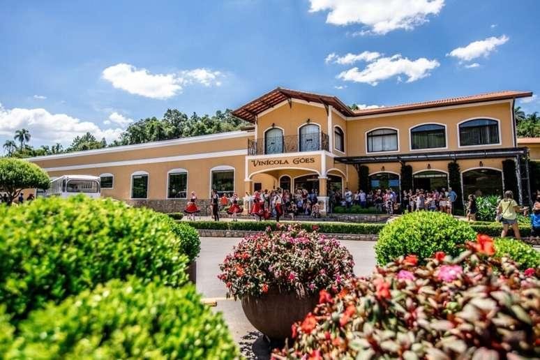 Fachada amarela da Vinícola Góes, em São Roque, com visitantes e canteiros floridos