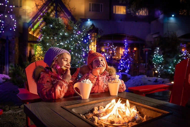 Duas pessoas junto à lareira externa diante da decoração de Natal no Fairmont Château Whistler.