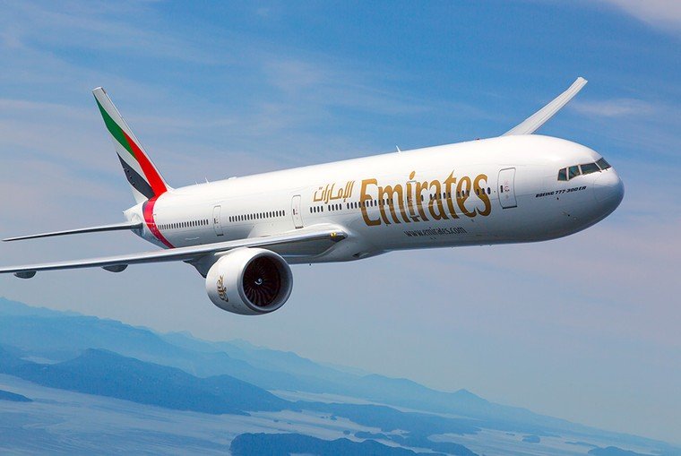 Avião da Emirates em voo sobre uma paisagem montanhosa.