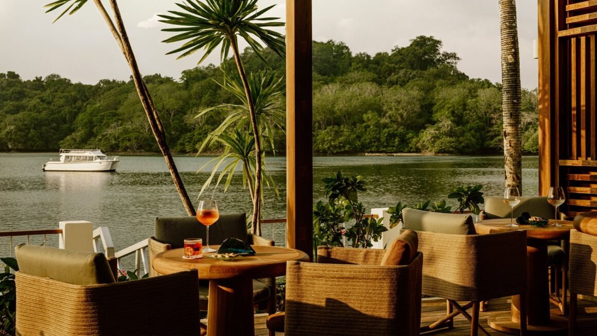 Terraço do M-Dock com poltronas de fibra natural e drinques diante da lagoa de Koror, com barco ao fundo