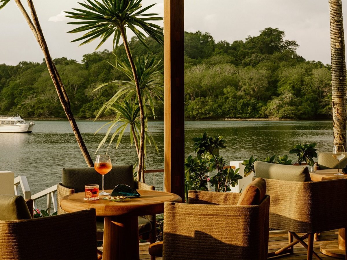 Terraço do M-Dock com poltronas de fibra natural e drinques diante da lagoa de Koror, com barco ao fundo