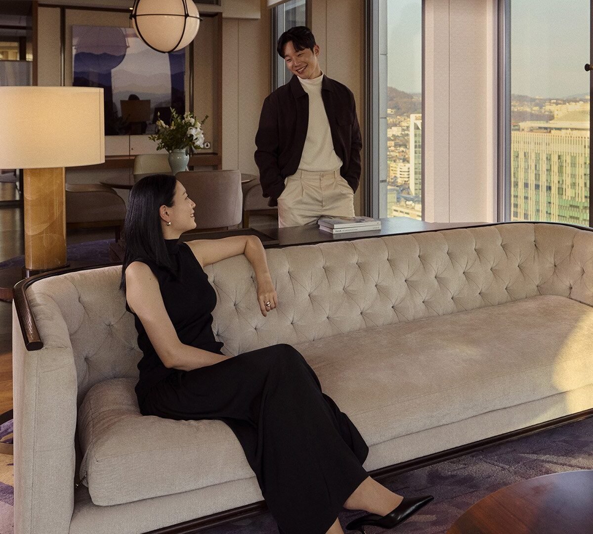 Casal em sala de estar de suíte do Four Seasons Hotel Seoul, com sofá capitonê, luneta e vista para a cidade