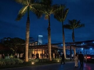 Convidados em traje de gala chegam à Casa Fasano à noite, entre palmeiras iluminadas