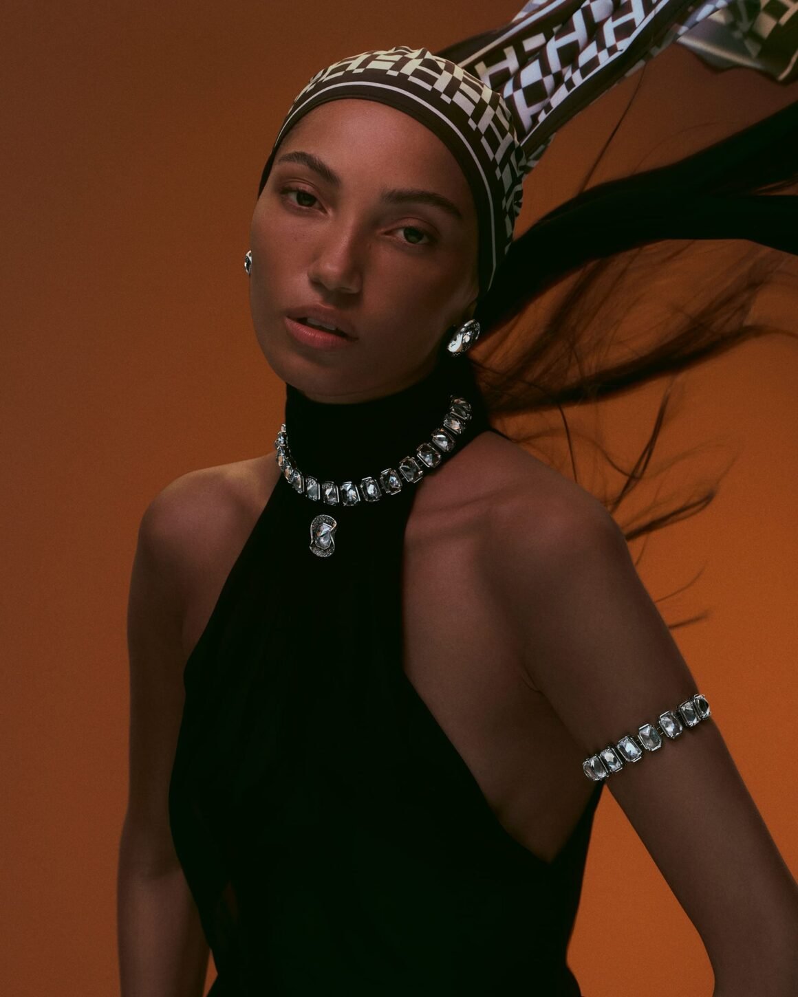 Model in a checkered headscarf and black halter top wearing a crystal choker with pendant, stud earrings and a crystal armlet