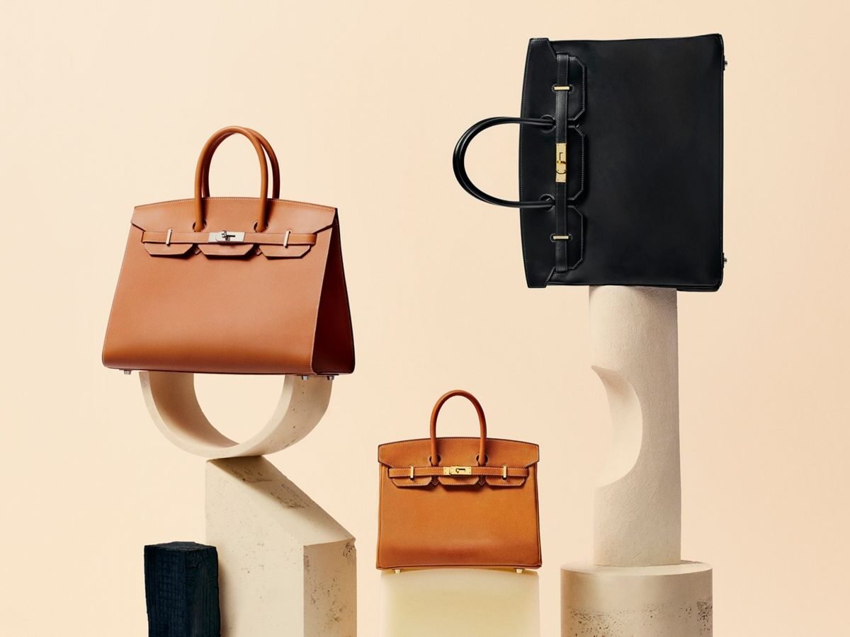 Três bolsas Birkin da Hermès, em couro caramelo e preto, sobre pedestais de pedra
